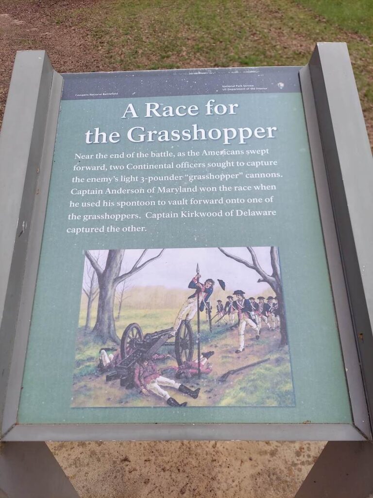 A sign along the tour of the Cowpens National Battlefield. The sign reads: A race for the grasshopper. Near the end of the battle, as the Americans swept forward, two Continental officers sought to capture the enemy’s light 3-pounder “grasshopper” cannons. Captain Anderson of Maryland won the race when he used his spontoon to vault forward onto one of the grasshoppers. Captain Kirkwood of Delaware captured the other.