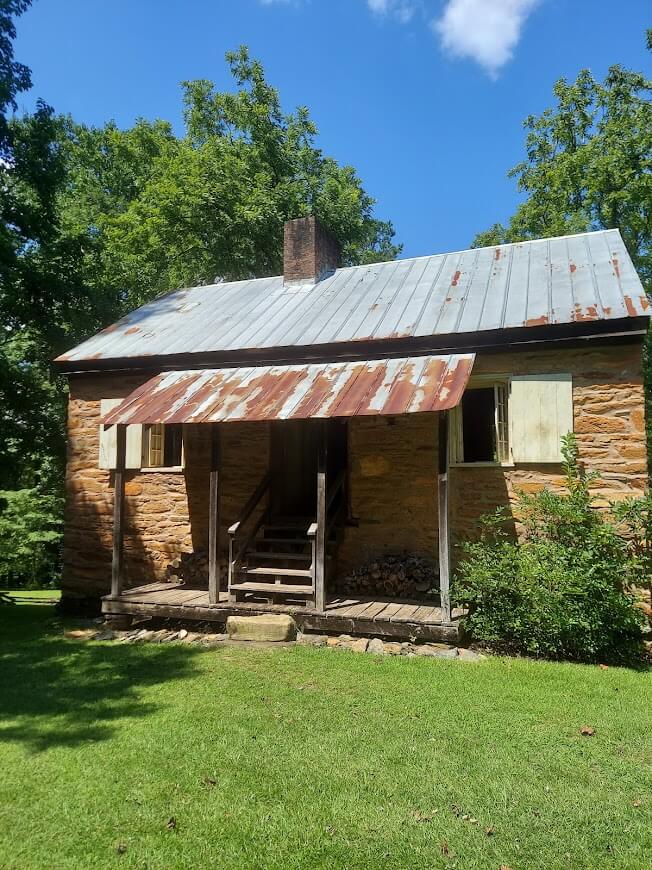 The front of the old yellow stone house at Oconee Station. There are wooden steps with a rusted metal roof that juts over the porch.