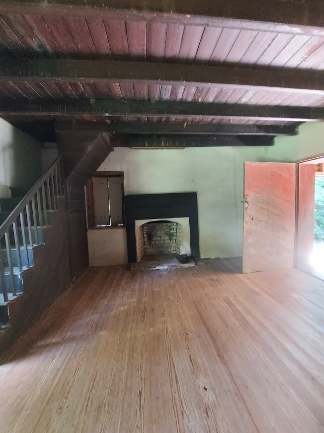 Inside the William Richards house. There is a fireplace in the center, a staircase to the left and an open door on the right.