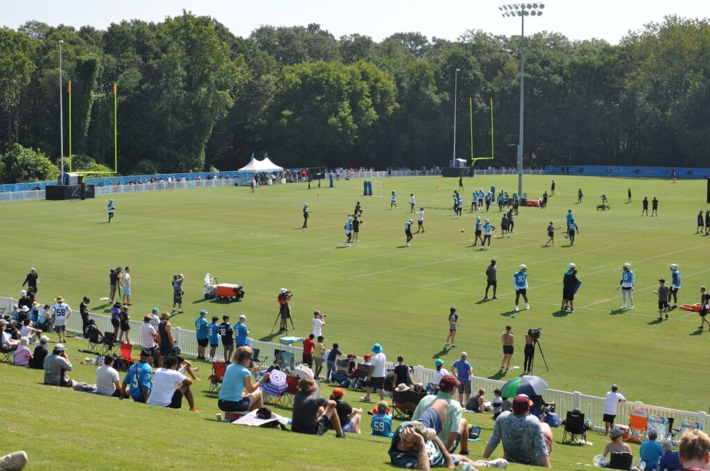 People sitting on the side of a hill and standing along a fence line to watch the Carolina Panthers practice at Wofford College.