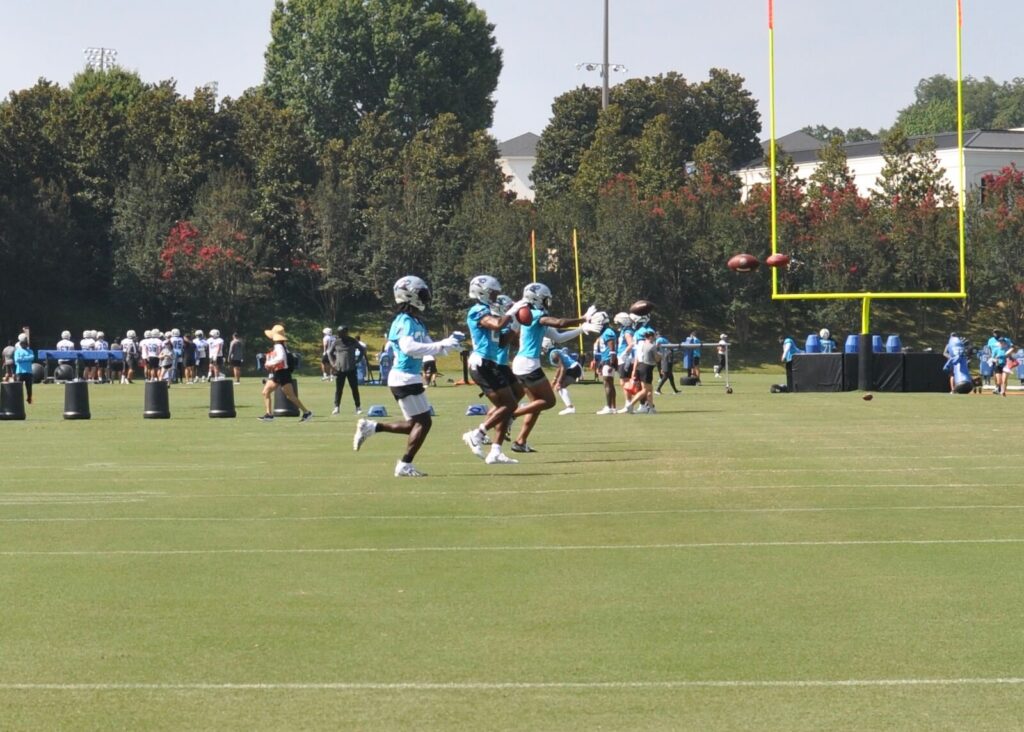Carolina Panthers catch footballs on a practice field at Wofford College.